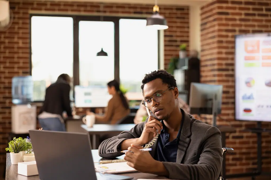 Una persona atiende una llamada mientras toma notas frente a su ordenador.