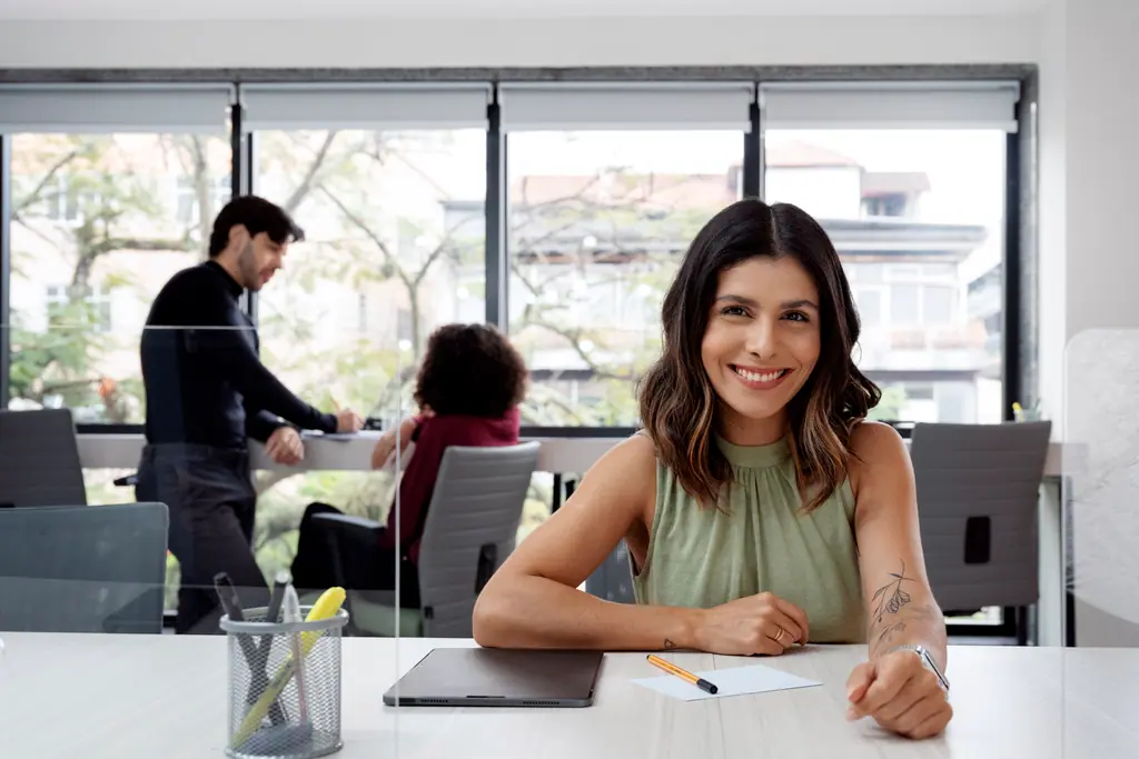 Una persona toma notas en una mesa de reuniones mientras sus compañeros trabajan al fondo.